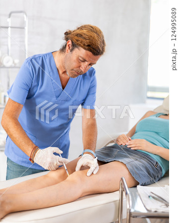 Male doctor making injection in leg of woman patient Male doctor making injection in leg of woman patient 124995089