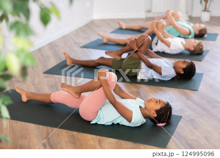 Girls and boys doing abdominal crunches with outstretched arms to strengthen abs and core muscles during group yoga class in studio Girls and boys doing abdominal crunches with outstretched arms to strengthen abs and core muscles during group yoga class in studio 124995096