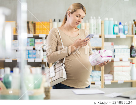 Pregnant woman in pharmacy scans QR code on feminine pad product 124995124