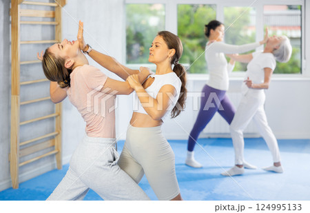 Woman and girl in gym perform basic elements of krav maga self-defense system. 124995133