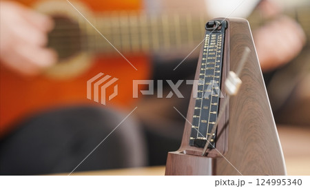 Metronome marking tempo while musician playing acoustic guitar Metronome marking tempo while musician playing acoustic guitar 124995340