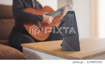 Musician practicing guitar using a metronome for perfect timing Musician practicing guitar using a metronome for perfect timing 124995363