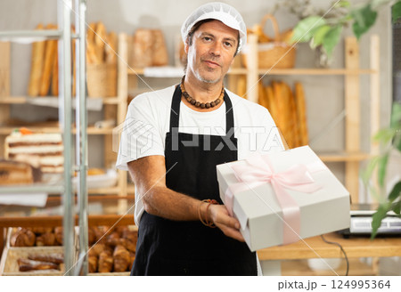 Middle-aged salesman holding cake box in bakery 124995364