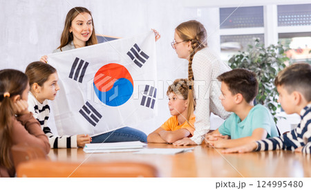 Schoolchildren listen carefully to story about the country South Korea. Teacher holds flag of South Korea in her hands Schoolchildren listen carefully to story about the country South Korea. Teacher holds flag of South Korea in her hands 124995480