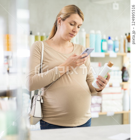 Pregnant woman in pharmacy scans QR code on hair loss shampoo product Pregnant woman in pharmacy scans QR code on hair loss shampoo product 124995516