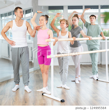 Teenage boys and girls practicing third position of ballet in dancehall Teenage boys and girls practicing third position of ballet in dancehall 124995564