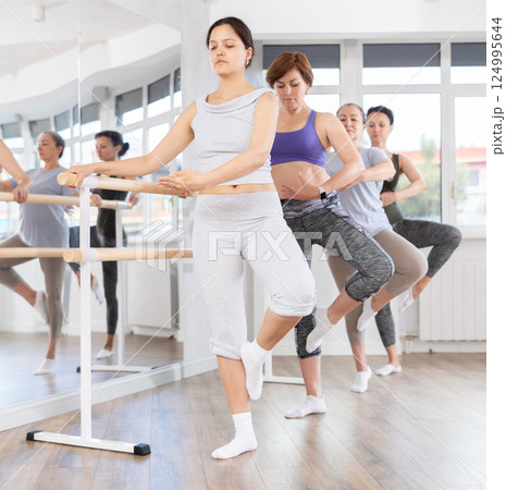 Group of female beginners performing fondue at barre 124995644
