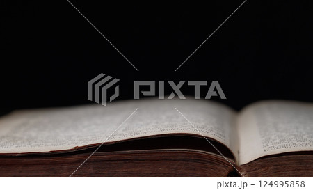 Side View of Old Open Book on table in library. Worn Pages. Ancient writings 124995858