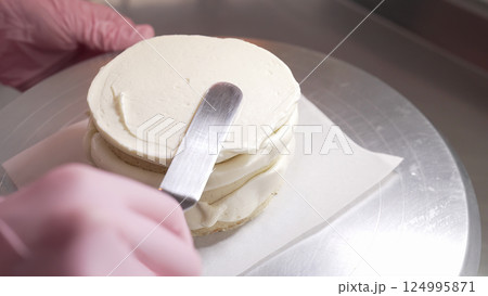 Pastry chef leveling cake sides with cream. Confectioner working with spatula. 124995871