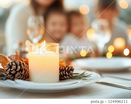 warm family gathering around beautifully set table with glowing candle, pinecones, and autumn leaves, creating cozy atmosphere 124996211