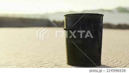 Trash bin sits on sandy beach at sunset with gentle waves in background 124996836