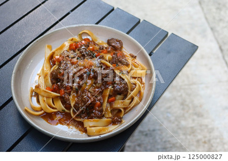 close up of Stewed Beef red wine sauce fettuccine pasta on an outdoor camping table with copy space 125000827