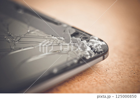 Shattered smartphone screen lying on surface, revealing potential repair costs and device vulnerability from accidental damage 125000850