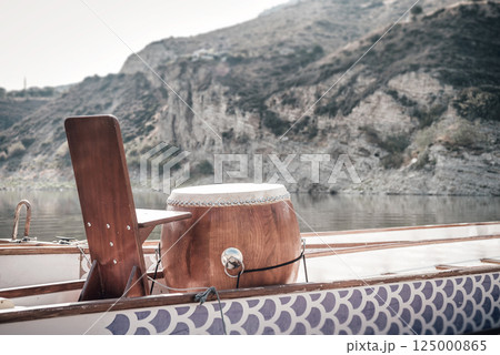 Wooden drum positioned strategically on Dragon Boat, signaling racing rhythm against mountainous lake landscape 125000865