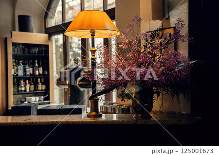 A warmly lit bar interior with an elegant table lamp, a lush bouquet of pink flowers, and a stylish A warmly lit bar interior with an elegant table lamp, a lush bouquet of pink flowers, and a stylish 125001673