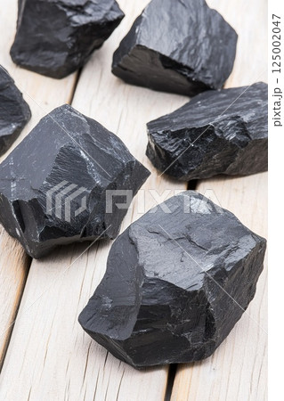 Raw black coal rocks on wooden surface displaying natural texture. 125002047