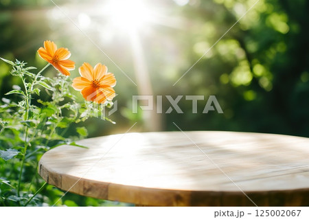 Sunlit orange flowers beside a wooden round table in a green garden. 125002067