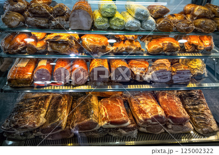 Various hams, bacons and deli meats in vacuum packaging close-up in glass display case of butcher shop. Various hams, bacons and deli meats in vacuum packaging close-up in glass display case of butcher shop. 125002322