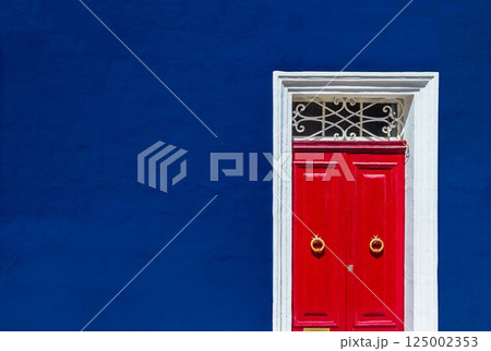 High contrast photograph of dark blue wall of residential building facade with red door High contrast photograph of dark blue wall of residential building facade with red door 125002353