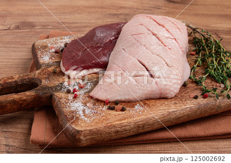 Fresh raw duck breasts, on a wooden chopping board, with herbs and spices, no people 125002692