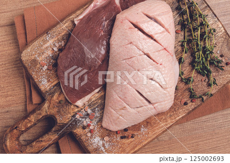 Fresh raw duck breasts, on a wooden chopping board, with herbs and spices, no people 125002693