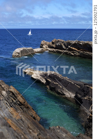 Sailing boat in blue sea near rocky coastline with crystal-clear turquoise azure waters, Ribadesella, Asturias, Spain, sunny day 125002701