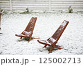 Wooden deck chairs covered with fresh snow in backyard garden after unexpected spring snowfall 125002713