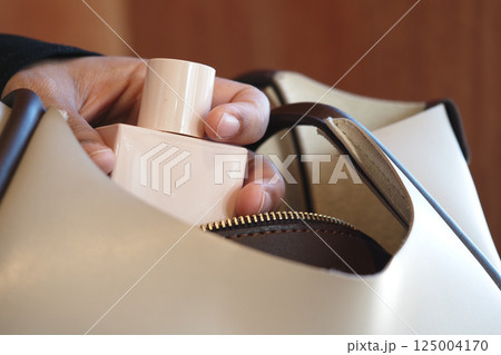 Hand placing perfume bottle into a stylish handbag 125004170