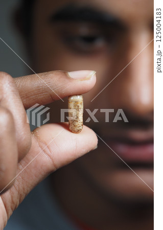 Holding a capsule with curiosity in a close-up Holding a capsule with curiosity in a close-up 125004183