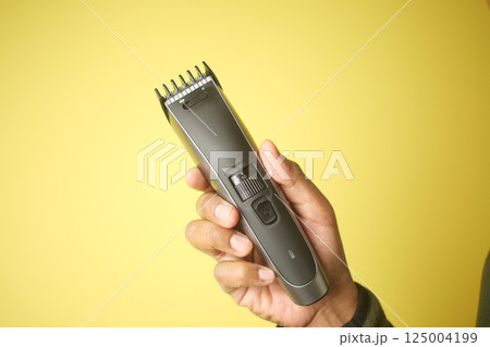 Hand holding hair clipper against a bright yellow backdrop Hand holding hair clipper against a bright yellow backdrop 125004199