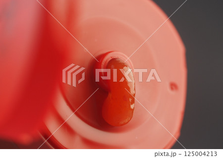 Bright red condiment squeezed from bottle cap Bright red condiment squeezed from bottle cap 125004213