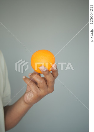 Holding a bright orange fruit in hand against a plain background Holding a bright orange fruit in hand against a plain background 125004215
