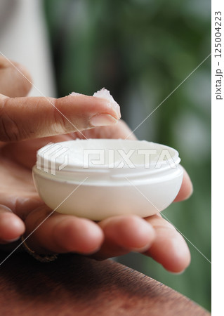 Hand applying petroleum jelly from white container in indoor setting Hand applying petroleum jelly from white container in indoor setting 125004223