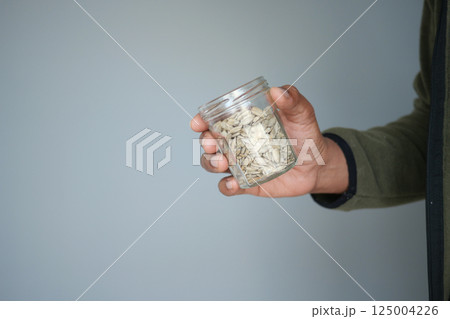 Hand holding a jar filled with seeds against a light background Hand holding a jar filled with seeds against a light background 125004226