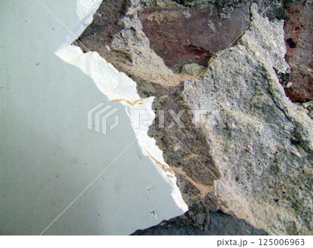 Layers of paint and plaster are exposed on a worn wall, showcasing texture and age. The remnants reveal insights into the history of this old building during the afternoon. 125006963