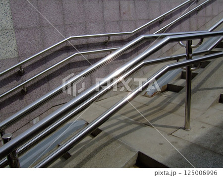 A set of metallic handrails alongside smooth concrete stairs supports safe navigation in an urban environment, highlighting modern architectural design and accessibility features. A set of metallic handrails alongside smooth concrete stairs supports safe navigation in an urban environment, highlighting modern architectural design and accessibility features. 125006996