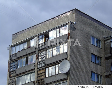 A multi-story building displays significant wear, with broken windows and damaged exterior. Reflections of clouds can be seen on the glass, indicating an overcast day. 125007000