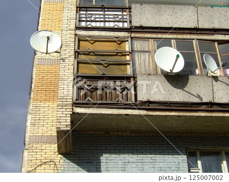 An old apartment building features distinctive architectural details and multiple satellite dishes attached to its balconies. The structure reflects the urban environment and history. 125007002