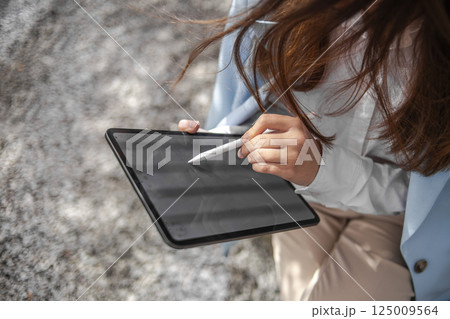 Woman using a tablet with a digital pen outdoors 125009564