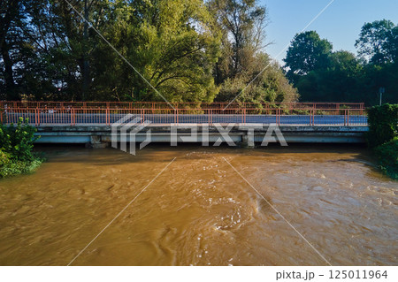 Brown muddy water flows under road bridge. Flooded river after heavy rainfall. Natural disaster Brown muddy water flows under road bridge. Flooded river after heavy rainfall. Natural disaster 125011964