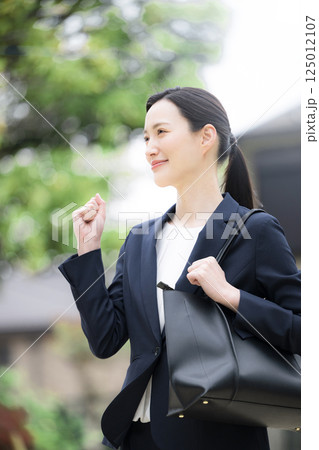 新緑の屋外でビジネススーツを着て営業や外回りのイメージの女性 ガッツポーズ 新緑の屋外でビジネススーツを着て営業や外回りのイメージの女性 ガッツポーズ 125012107