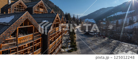Wooden chalet style Alpine hotel with steep roofs, near a winding road, snow dusted trees, mountains, a bus, and people in Dolomites, Italy. Wooden chalet style Alpine hotel with steep roofs, near a winding road, snow dusted trees, mountains, a bus, and people in Dolomites, Italy. 125012248