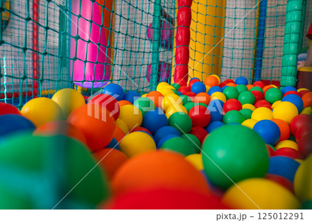 Vibrant play area featuring a colorful ball pit with red, yellow, green, blue, and orange balls, surrounded by a safety net and padded structures. 125012291