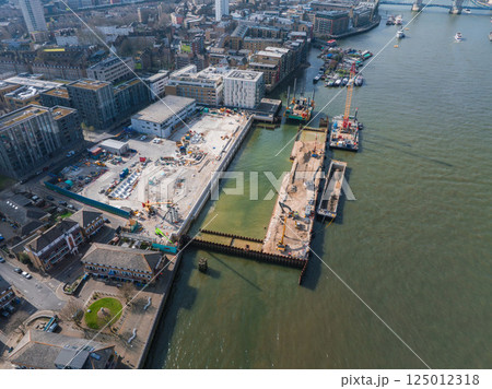 Aerial image of Tower Bridge and River Thames with cranes at a construction site, modern and older buildings, green space, and active boats. Aerial image of Tower Bridge and River Thames with cranes at a construction site, modern and older buildings, green space, and active boats. 125012318
