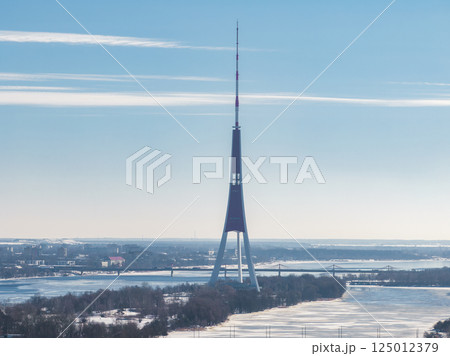 The Riga TV Tower stands on an island in the Daugava River, surrounded by snow and frozen water, with Riga's cityscape and bridges in the background. The Riga TV Tower stands on an island in the Daugava River, surrounded by snow and frozen water, with Riga's cityscape and bridges in the background. 125012379