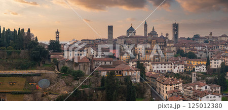 View of Bergamo's old town in Italy during sunset, featuring the Campanone, Basilica of Santa Maria Maggiore, medieval architecture, and lush greenery. View of Bergamo's old town in Italy during sunset, featuring the Campanone, Basilica of Santa Maria Maggiore, medieval architecture, and lush greenery. 125012380