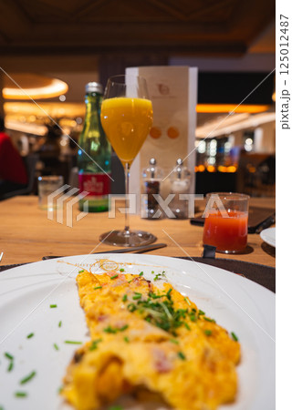 Close up of a plate with a herb garnished omelet, orange juice, and sparkling water on a wooden table in a modern, upscale dining area in Austria. 125012487