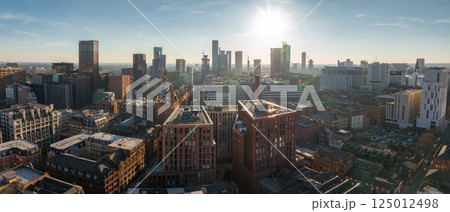 Aerial view of Manchester, UK, on a sunny day, featuring skyscrapers, construction cranes, historic brick buildings, and modern architecture. 125012498