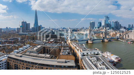 Aerial view of Tower Bridge over the River Thames, the Shard, and modern City of London buildings under a clear blue sky with scattered clouds. 125012525