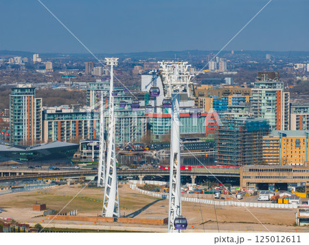 Aerial view of London featuring Emirates Air Line cable cars over the Thames, modern buildings, the O2 Arena, and urban construction areas. 125012611